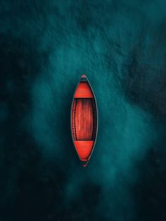 an aerial view of a red boat in the middle of dark blue water with clouds