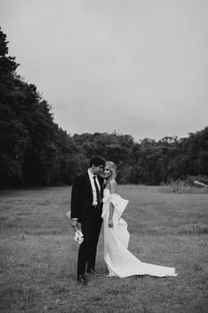 black and white photo of bride and groom standing in the grass with trees behind them