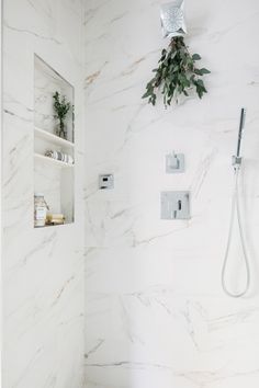 a bathroom with white marble walls and flooring, including a shower head mounted on the wall