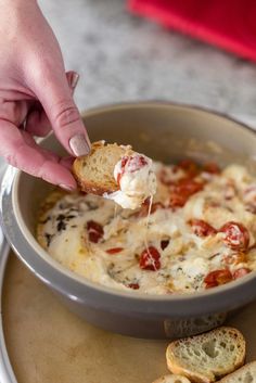 a person dipping some bread into a bowl filled with cheese and tomato sauce on a plate