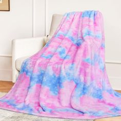 a pink and blue blanket sitting on top of a white couch next to a chair