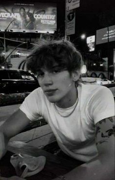 a young man sitting on top of a wooden bench in front of a street sign