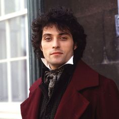 a man with black hair wearing a red jacket and bow tie, looking off into the distance