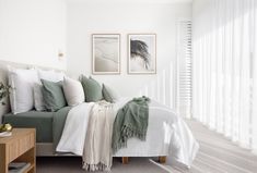 a bed with white sheets and green throw pillows