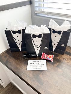 three paper bags with black and white tuxedos on them sitting on a table