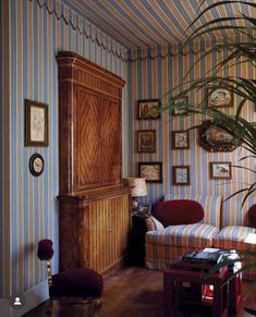 a living room with striped wallpaper and furniture in the corner, next to a large potted plant