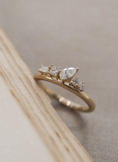 a gold ring with three pear shaped diamonds sitting on top of a piece of wood