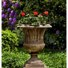 a planter with red flowers in it sitting on a stone pedestal next to some bushes