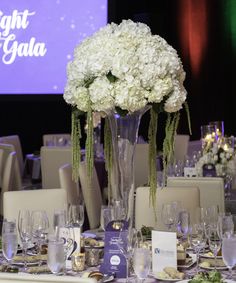 there is a large vase with flowers in it on top of a table set for an event