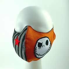 a white mannequin head wearing an orange and black face mask with a red star on it