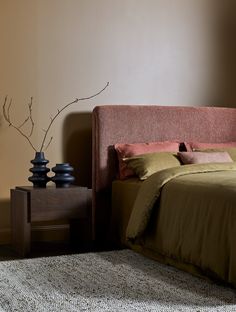 a bed sitting next to a night stand with two vases on top of it