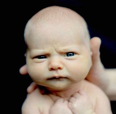 a close up of a baby being held by someone's hands with blue eyes