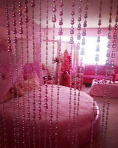 a pink bed sitting next to a window covered in beads