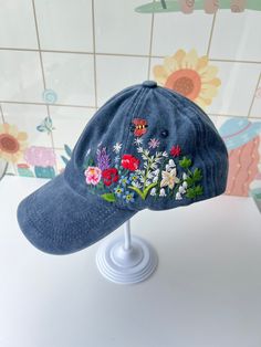 a blue hat with embroidered flowers on it sitting on top of a white stand in front of a tiled wall