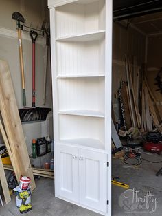 a tall white bookcase sitting inside of a garage next to tools and other items