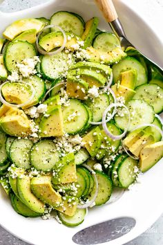 a white bowl filled with sliced cucumbers and topped with parmesan cheese