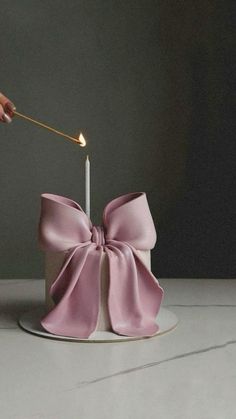 a person lighting a candle on top of a pink bow shaped cake with a stick in it