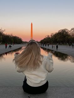 a woman sitting on the ground looking at an obelisk in washington d c