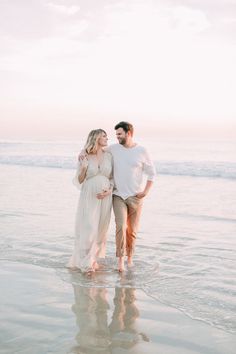 a pregnant couple standing in the ocean at sunset