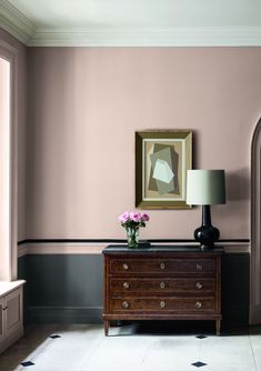 a living room with a dresser, lamp and painting on the wall in it's corner