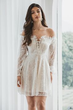 a woman standing in front of a window wearing a white dress with sheer lace detailing