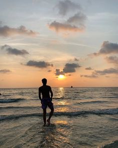 a man standing in the ocean at sunset