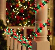 a christmas tree is lit up in front of a white fence with red and green lights