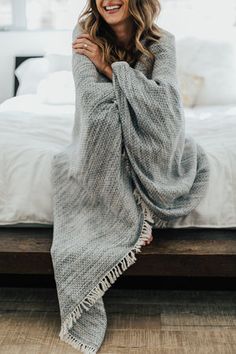 a smiling woman wrapped in a blanket sitting on a bed with her arms folded up