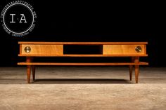 a wooden table sitting on top of a floor next to a black wall with a logo above it