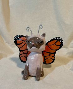 a cat figurine with a butterfly wings on it's head sitting on a white surface