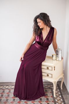 a woman in a long purple dress leaning on a small table and looking off to the side