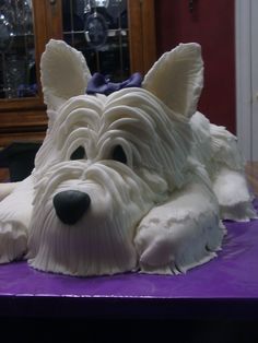 a cake shaped like a dog laying on top of a purple tablecloth covered in icing