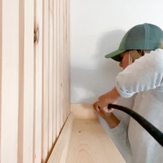 a woman in a green hat is using a vacuum to clean the wood on the wall