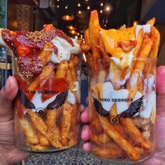 two people holding up glasses filled with french fries covered in sauce and ketchup