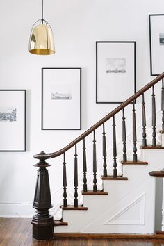 a staircase with pictures on the wall next to it and a light fixture hanging from the ceiling