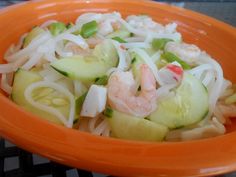 an orange bowl filled with noodles, shrimp and cucumber salad on top of a table