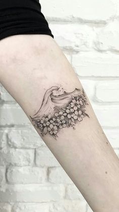 a woman's arm with flowers on it and a wave coming out of the water