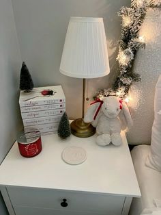 a white night stand with a lamp and some christmas decorations on it next to a stack of books