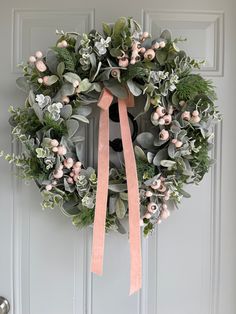 a wreath on the front door with pink ribbon and greenery hanging from it's side