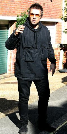 a man in black is walking down the street with his hand on his hip and wearing sunglasses