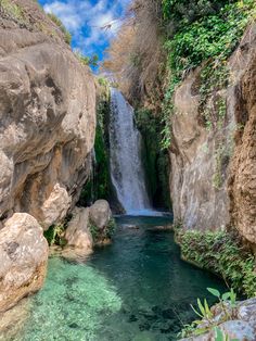 the waterfall is surrounded by large rocks and green vegetation