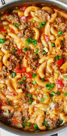 a skillet filled with pasta and meat in tomato sauce, topped with green onions