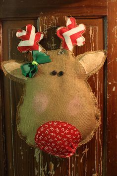 a burlap reindeer head hanging on a wooden door with red and green bows