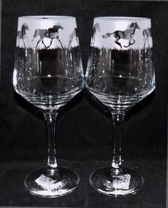 two wine glasses with horses painted on the glass are sitting side - by - side