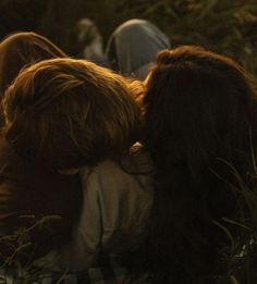 two people laying down in the grass with their heads on each other's shoulders