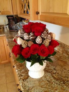 a white vase filled with red roses and chocolate covered strawberries on top of a counter