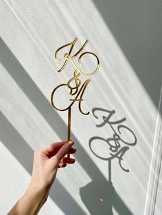 a hand holding a cake topper in the shape of a bike and letter m