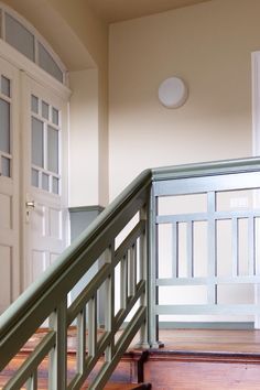 an empty room with wooden floors and green railings on the second floor, next to a white door