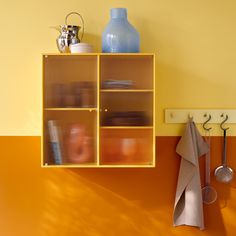 a yellow shelf with utensils hanging from it's sides and a blue vase on the wall