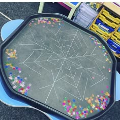 a black tray with colored chalk drawings on it and some plastic bins in the background